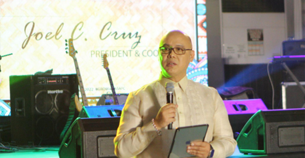 A man in a white shirt and glasses, Joel C. Cruz from South Asialink, speaking into a microphone.