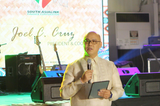 A man in a white shirt and glasses, Joel C. Cruz from South Asialink, speaking into a microphone.