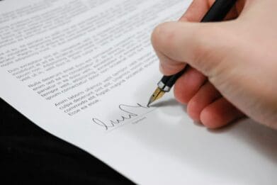 Hand signing a document with a pen on paper, representing an official or formal agreement