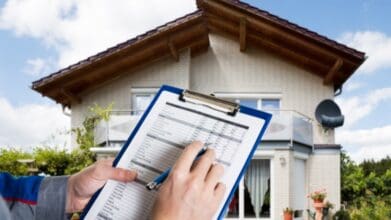 A loan officer assessing property documents on a clipboard in front of a house, symbolizing real estate-backed financing. This represents how Business Loans in the Philippines, including Sangla Titulo, provide financial support using land or property as collateral.
