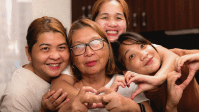 Three women hugging their elderly mom and making heart signs for Mother's Day 2025