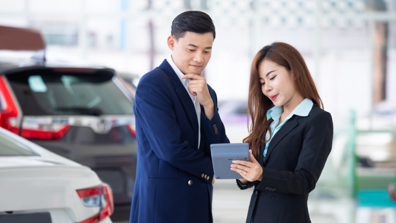 Car buyer discussing with dealer on tablet, highlighting negotiation in buying a secondhand car.