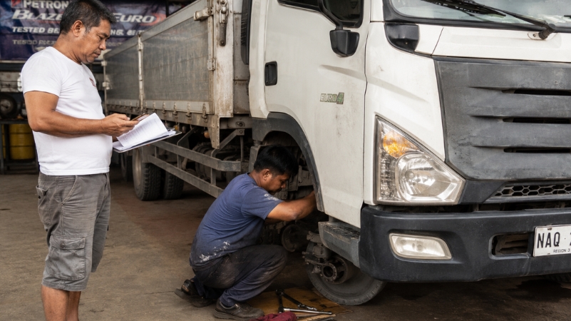Mechanic repairing a cargo truck while owner checks expenses